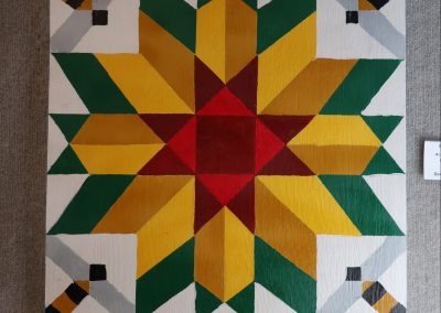 Bumble Bee - acrylic on wood a quilt pattern of green, yellow, red with geometric bees in the corners.